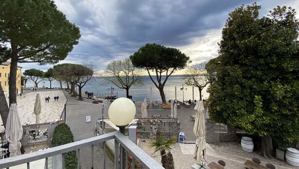 A seaside terrace with outdoor seating, a large white spherical light, and a view of the sea. - Hotel Astoria (Garda)