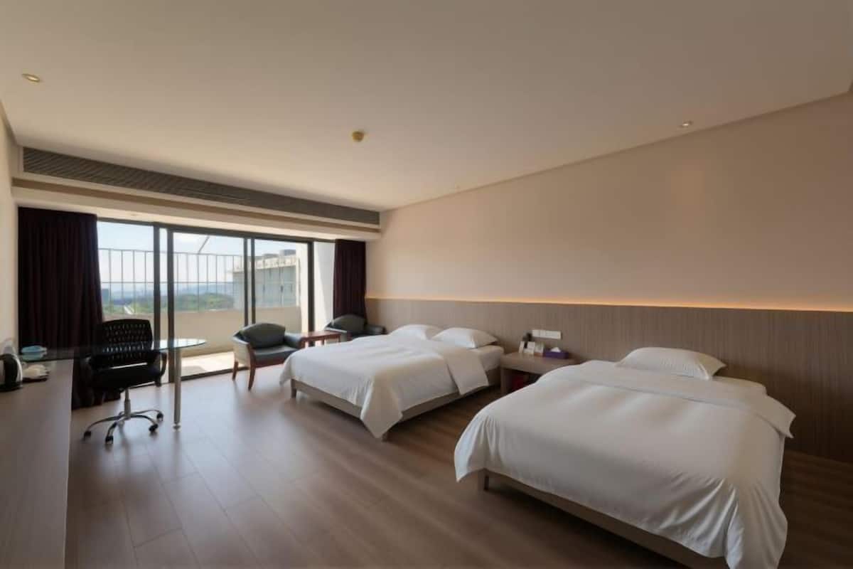 A hotel room with two beds, a desk, a chair, and a large window.