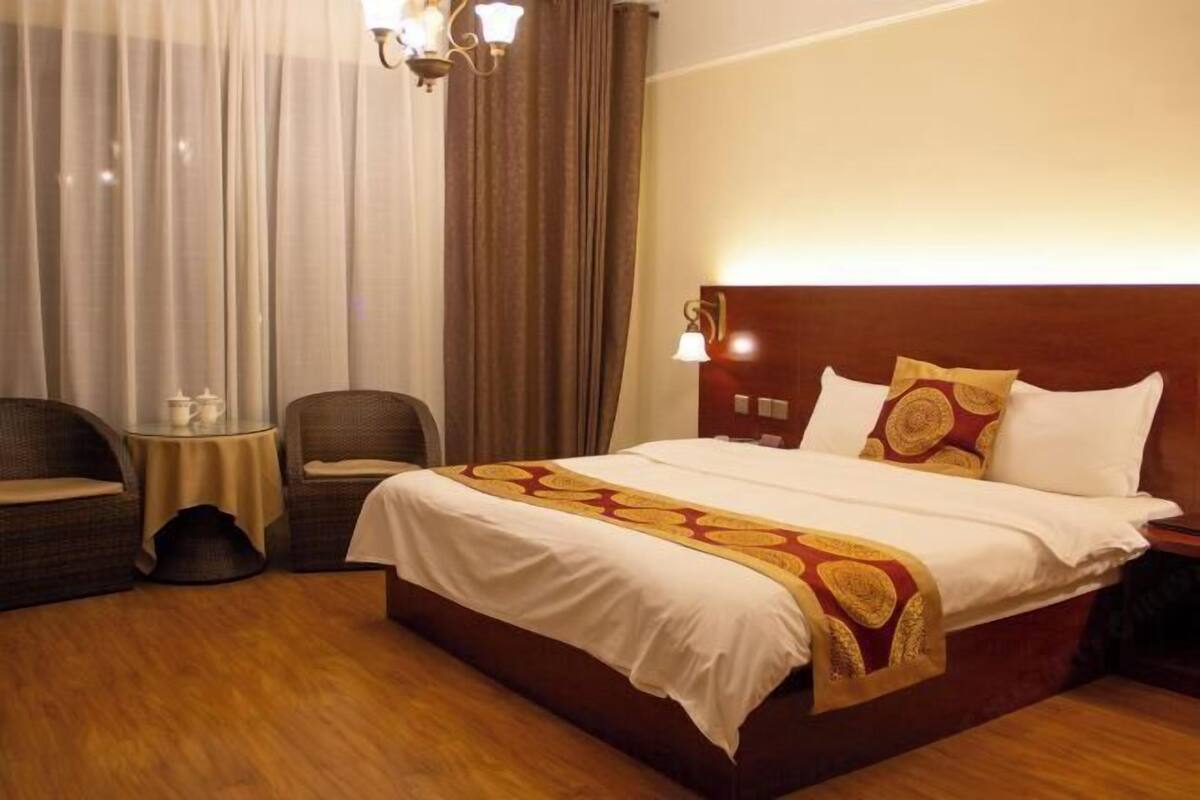 A hotel room with a large bed, two armchairs, a small round table, and a chandelier.