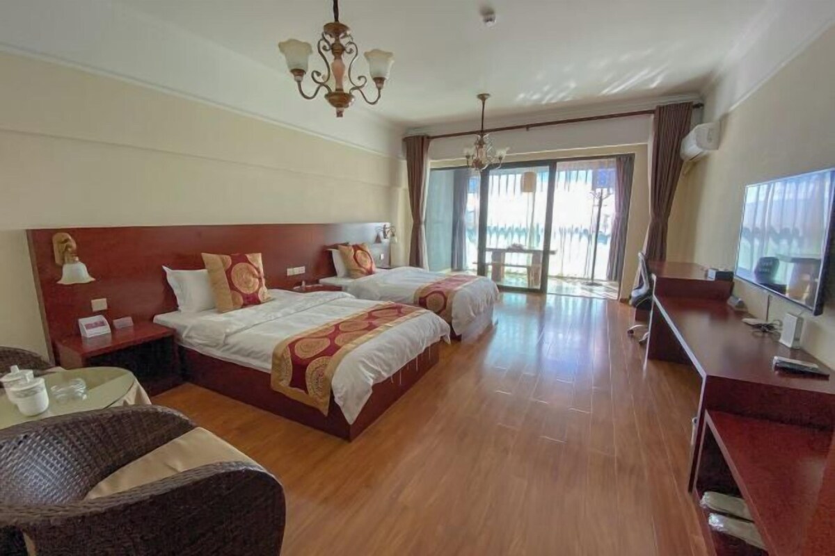 Ein Hotelzimmer mit zwei Betten, einem Schreibtisch, einem Stuhl, einem Fernseher und einem Balkon mit Vorhängen.