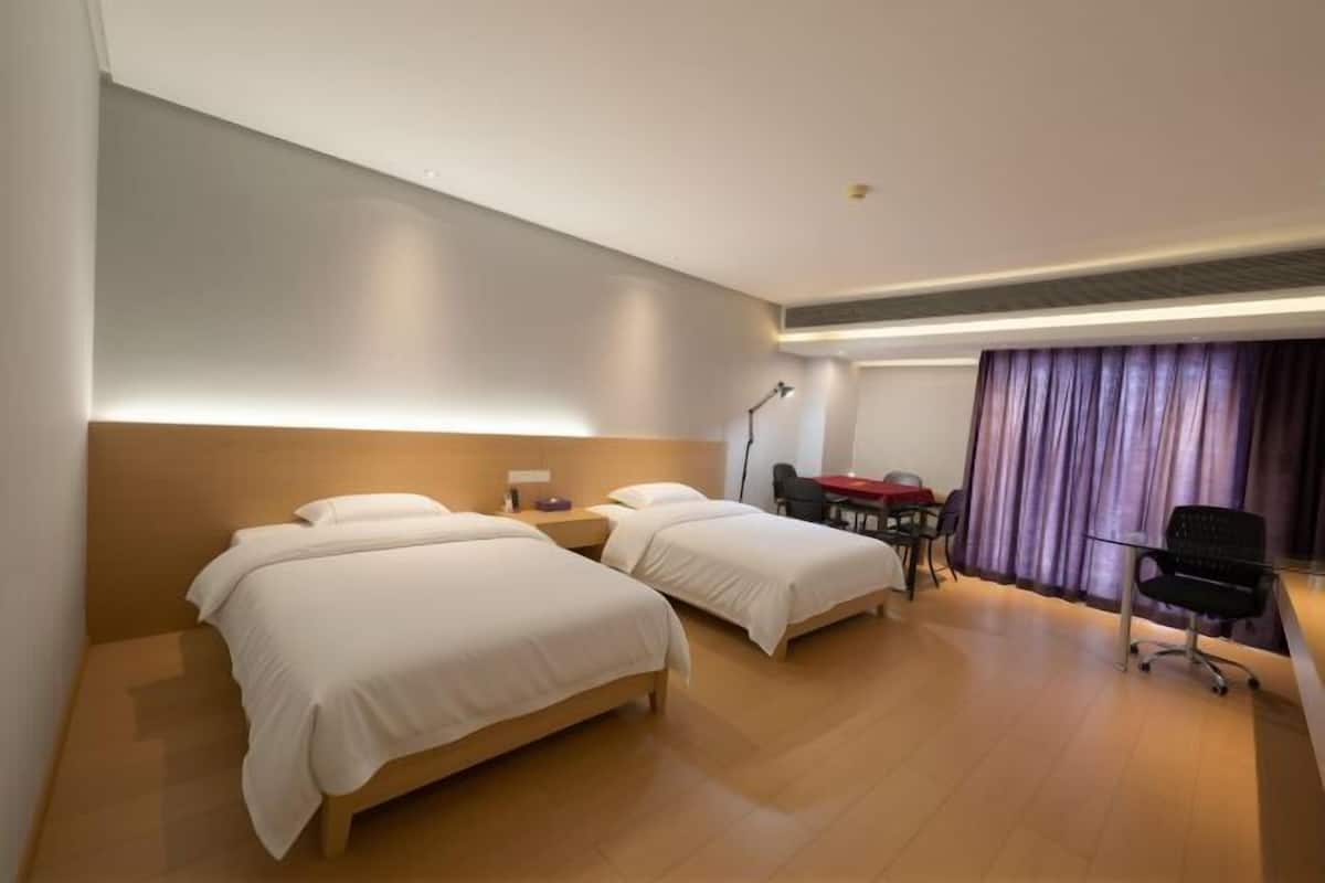 A hotel room with two beds, a desk, a chair, and a window with curtains.
