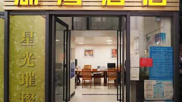 A hotel entrance with a reception desk, a dining area, and a visible menu board.