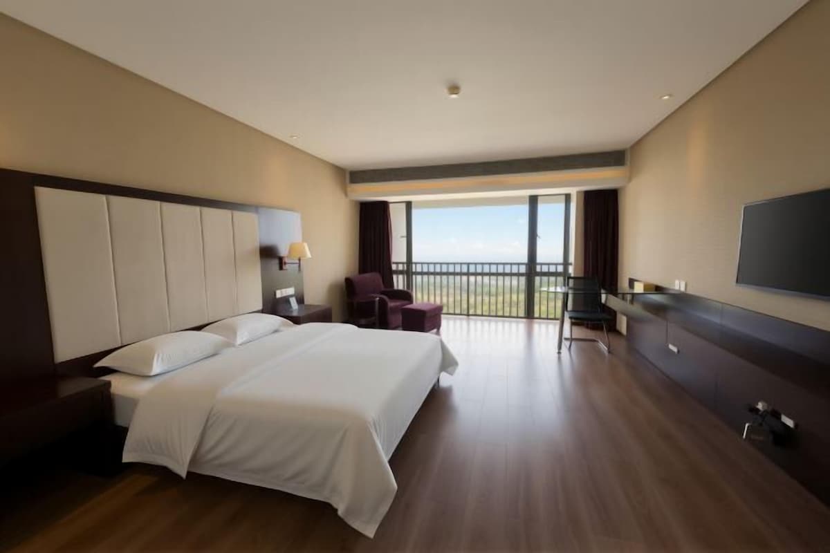 Quarto de hotel com uma cama grande, uma escrivaninha, uma cadeira e varanda com vista.