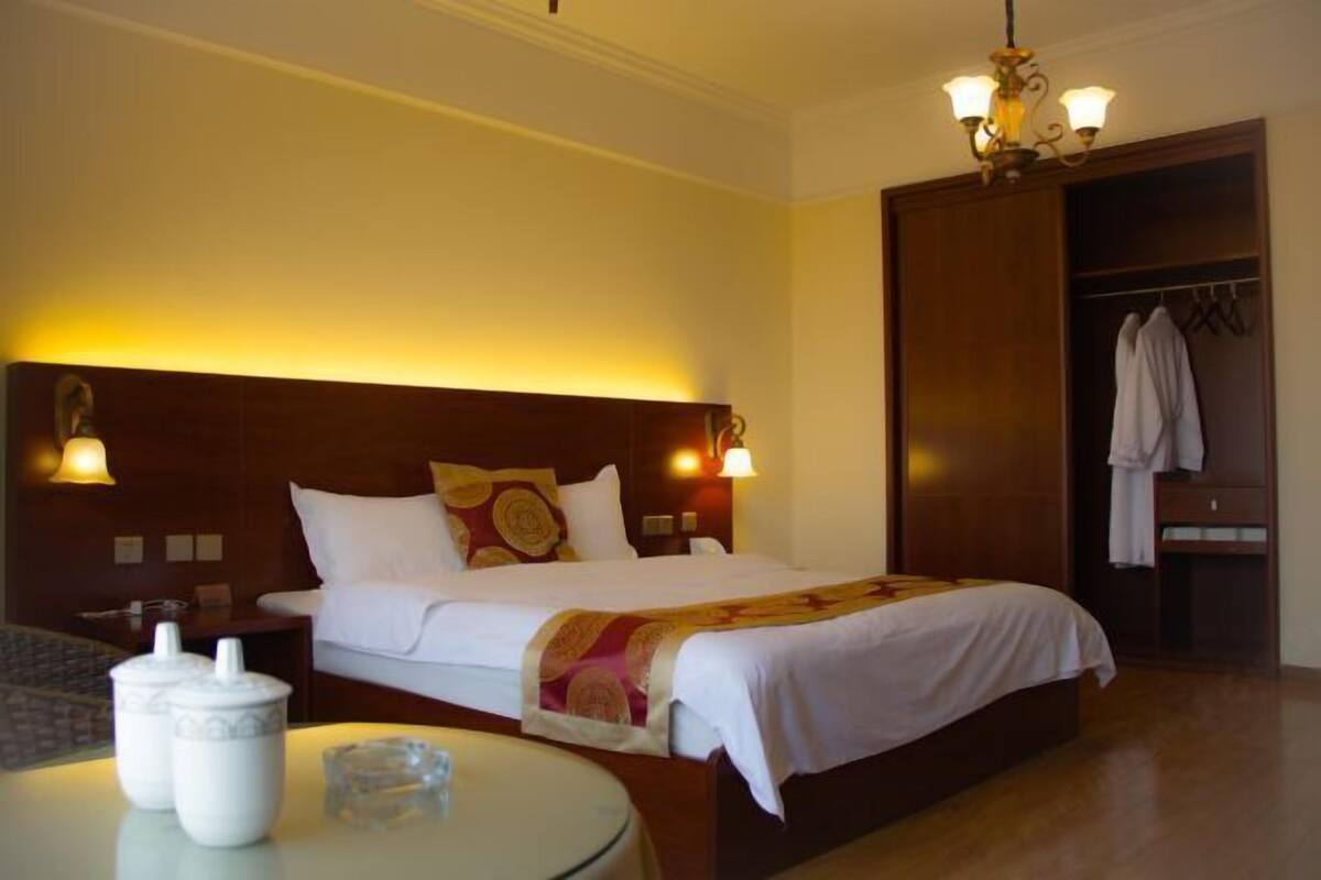 A hotel room with a large bed, bedside lamps, a wardrobe, and a round table with a glass top.