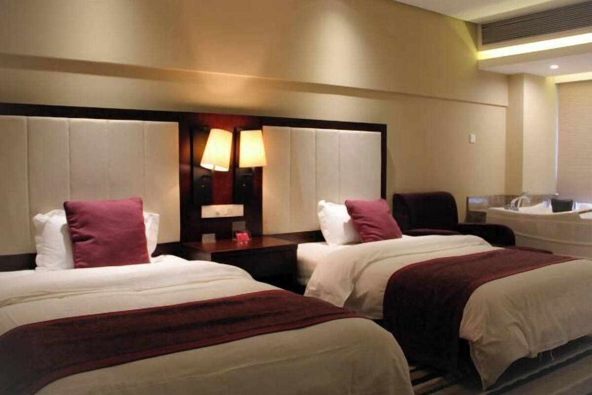 A hotel room with two beds, a large mirror, bedside lamps, a nightstand, and a bathroom with a bathtub.
