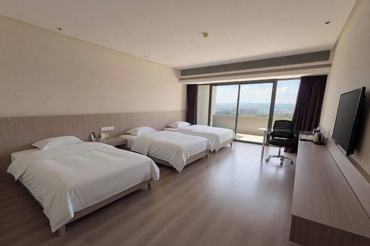 A hotel room with three beds, a desk, a chair, and a TV.