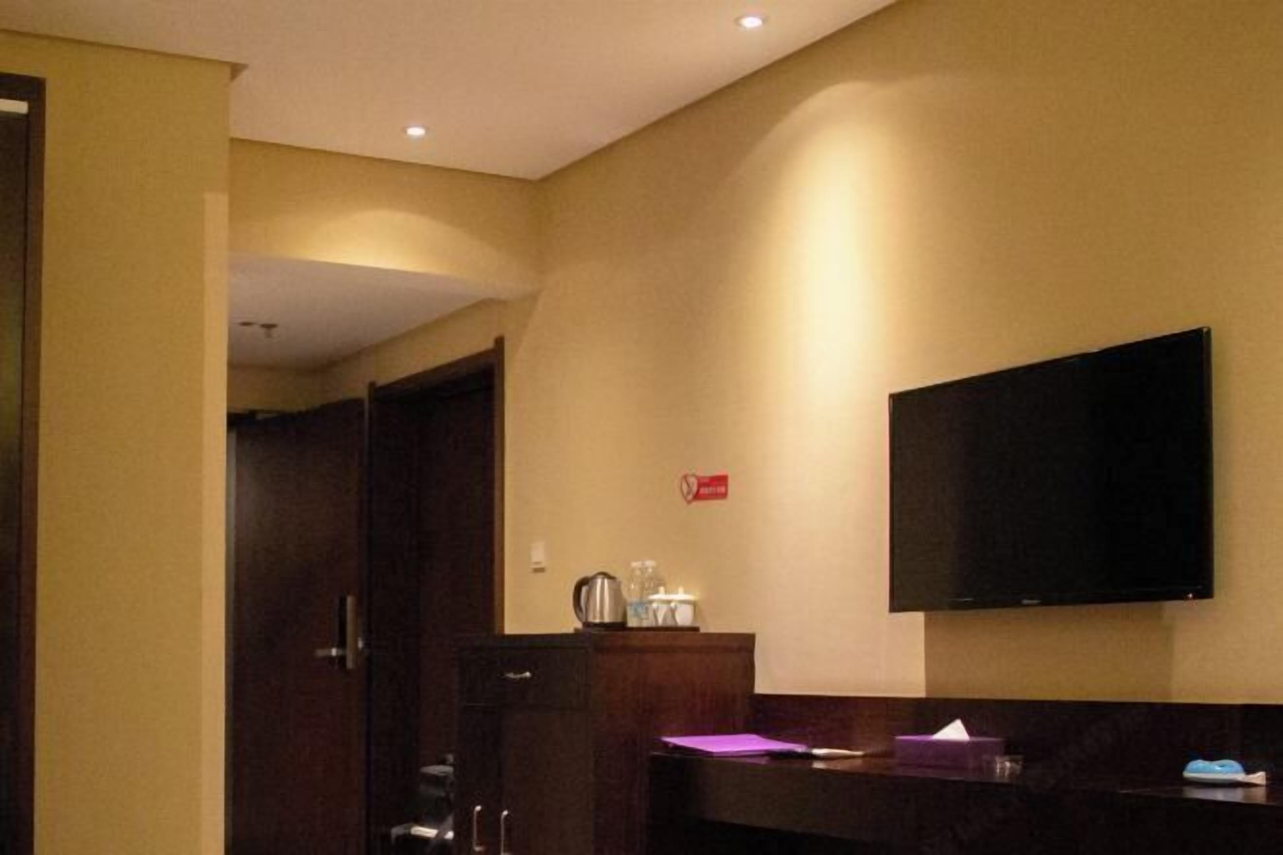 Habitación de hotel con televisión de pantalla plana montada en la pared, un mueble de madera y una puerta que da a otra habitación.