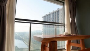 A room with a large window, a wooden table, and a view of a building and landscape. - Huwan Hotel (Anning)