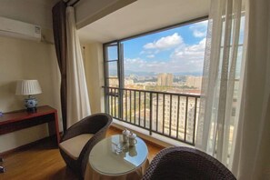 Ein Balkon mit Korbstühlen und einem kleinen Tisch, mit Blick auf eine Stadtlandschaft mit Gebäuden und blauem Himmel.