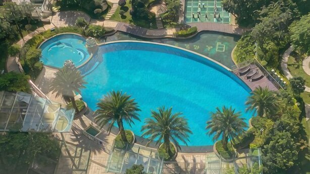 A large oval-shaped swimming pool surrounded by palm trees and a landscaped garden. - Huwan Hotel (Anning)