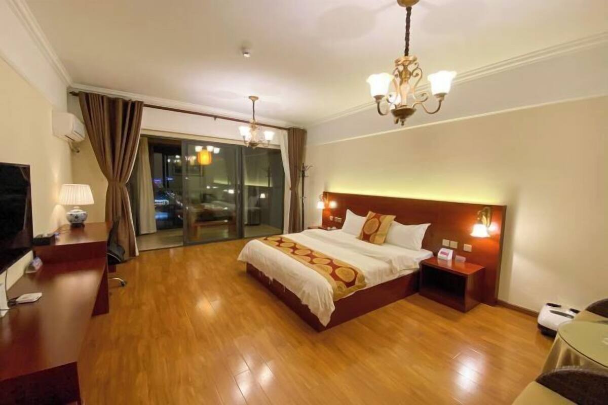 A hotel room with a large bed, a desk with a lamp, a TV, and a view of the city through the window.