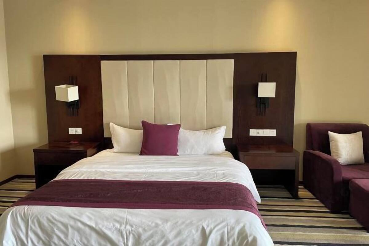 A hotel room with a large bed, two nightstands, a chair, and a headboard with built-in lighting.