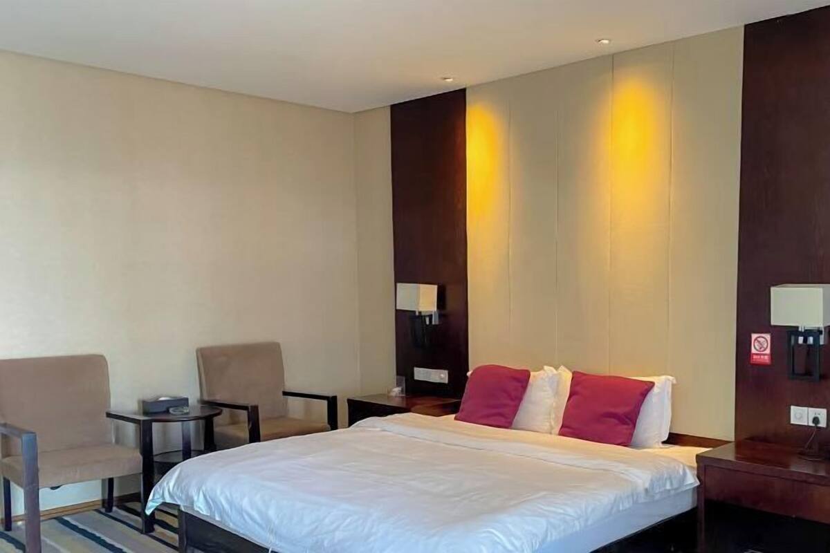 A hotel room with a bed, two chairs, a small table, a nightstand, and a wall-mounted lamp.