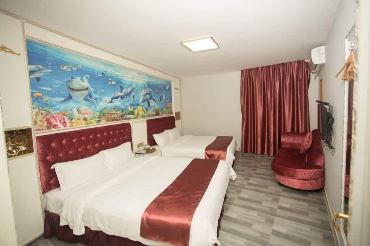Quarto de hotel com duas camas, uma poltrona de veludo vermelho, um mural com cena subaquática e uma cortina vermelha.