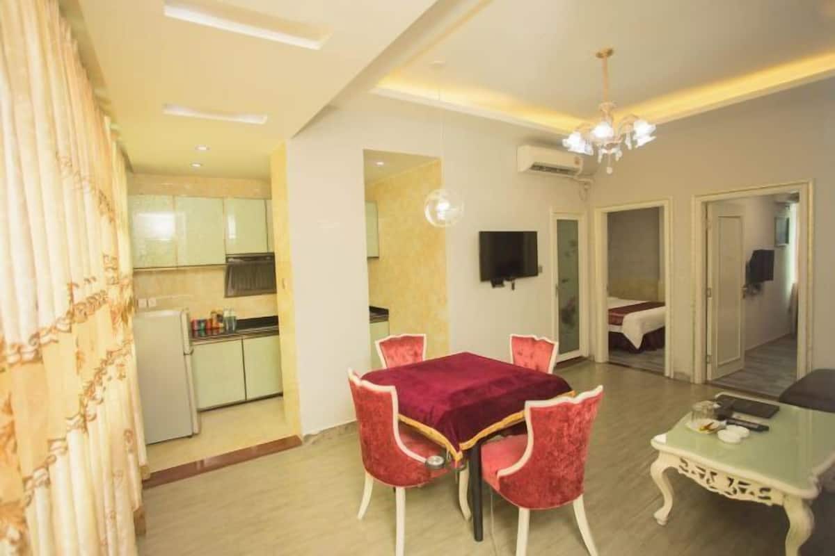 Uma área de refeições com mesa e cadeiras, uma pequena cozinha e uma televisão fixada na parede.