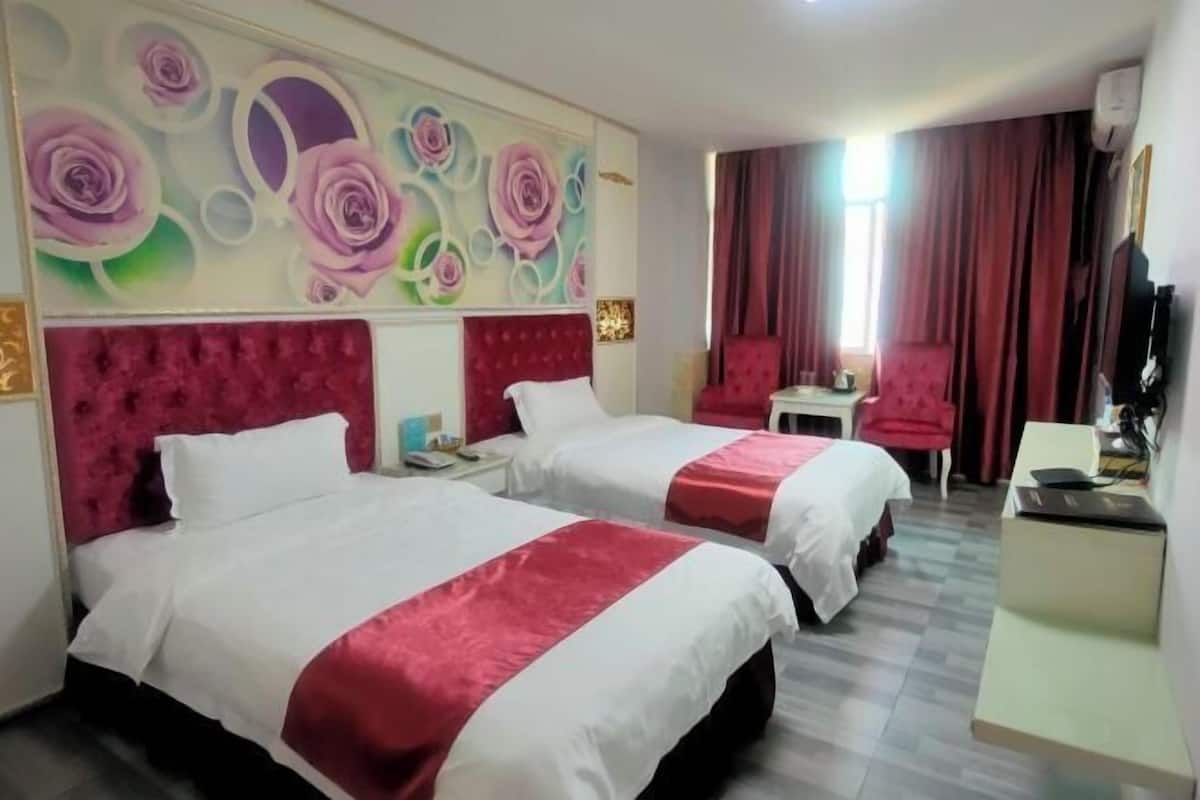 Quarto de hotel com duas camas, esquema de cores vermelho e branco, um mural floral na parede e cortina vermelha.