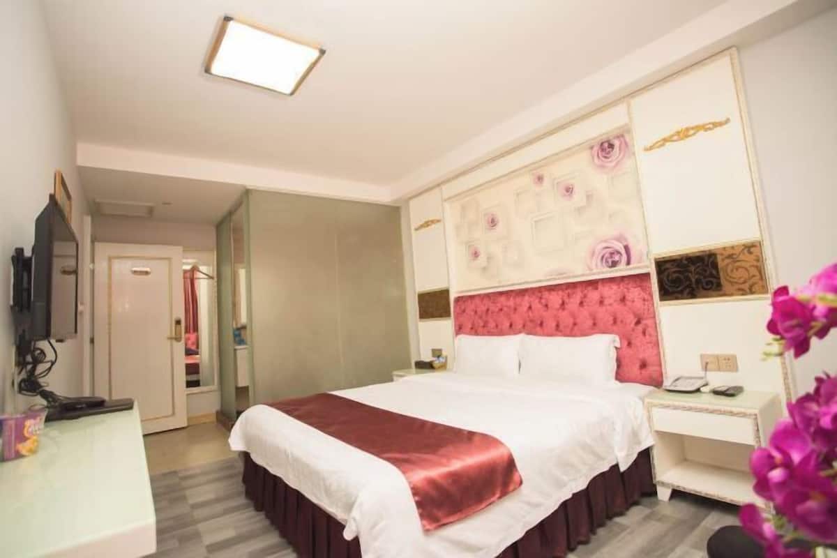 Quarto de hotel com uma cama grande, mesa de cabeceira, televisão e guarda-roupa.