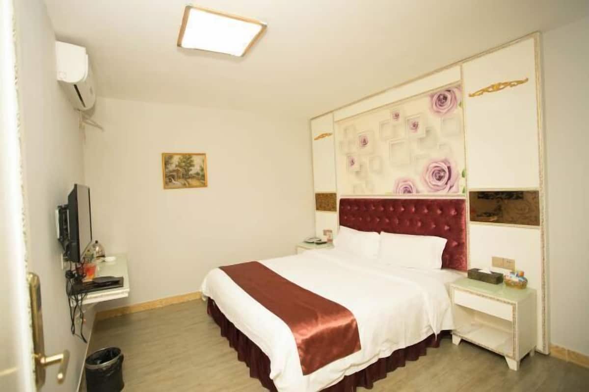Quarto de hotel com cama, mesas de cabeceira, televisão e um quadro na parede.