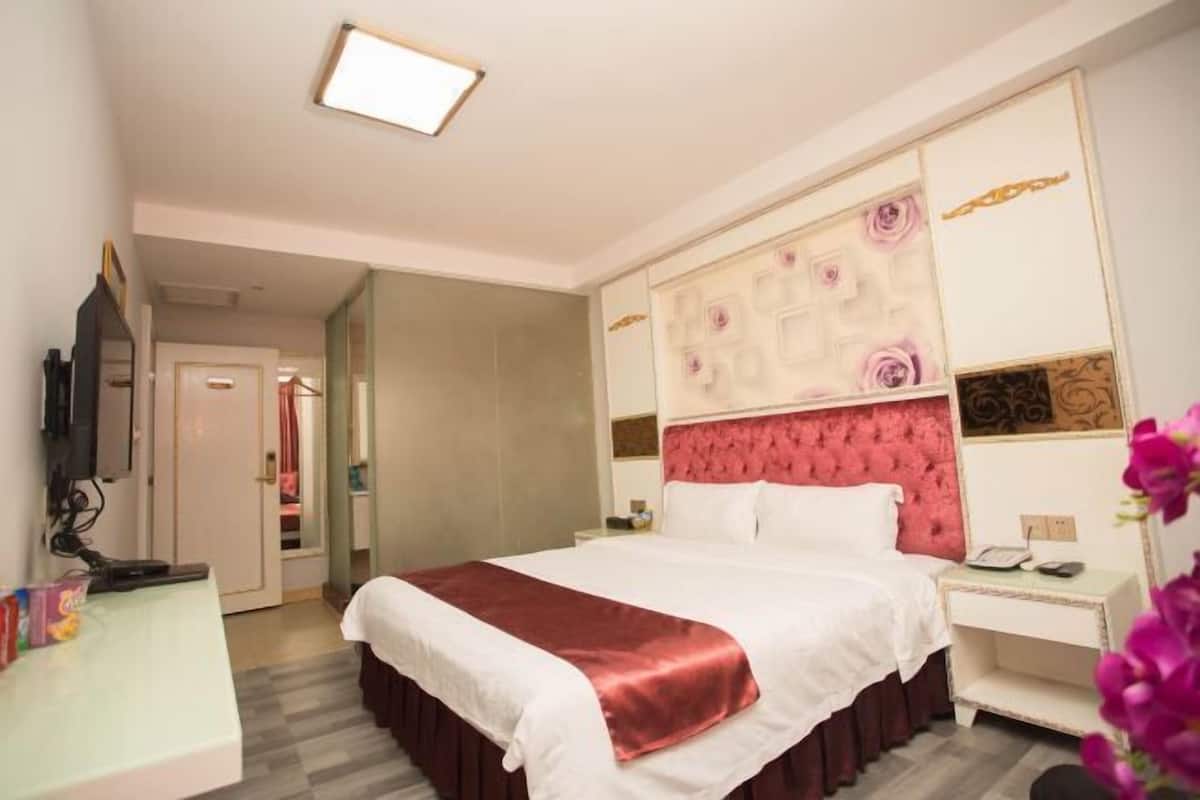 Quarto de hotel com cama, mesa de cabeceira e televisão.