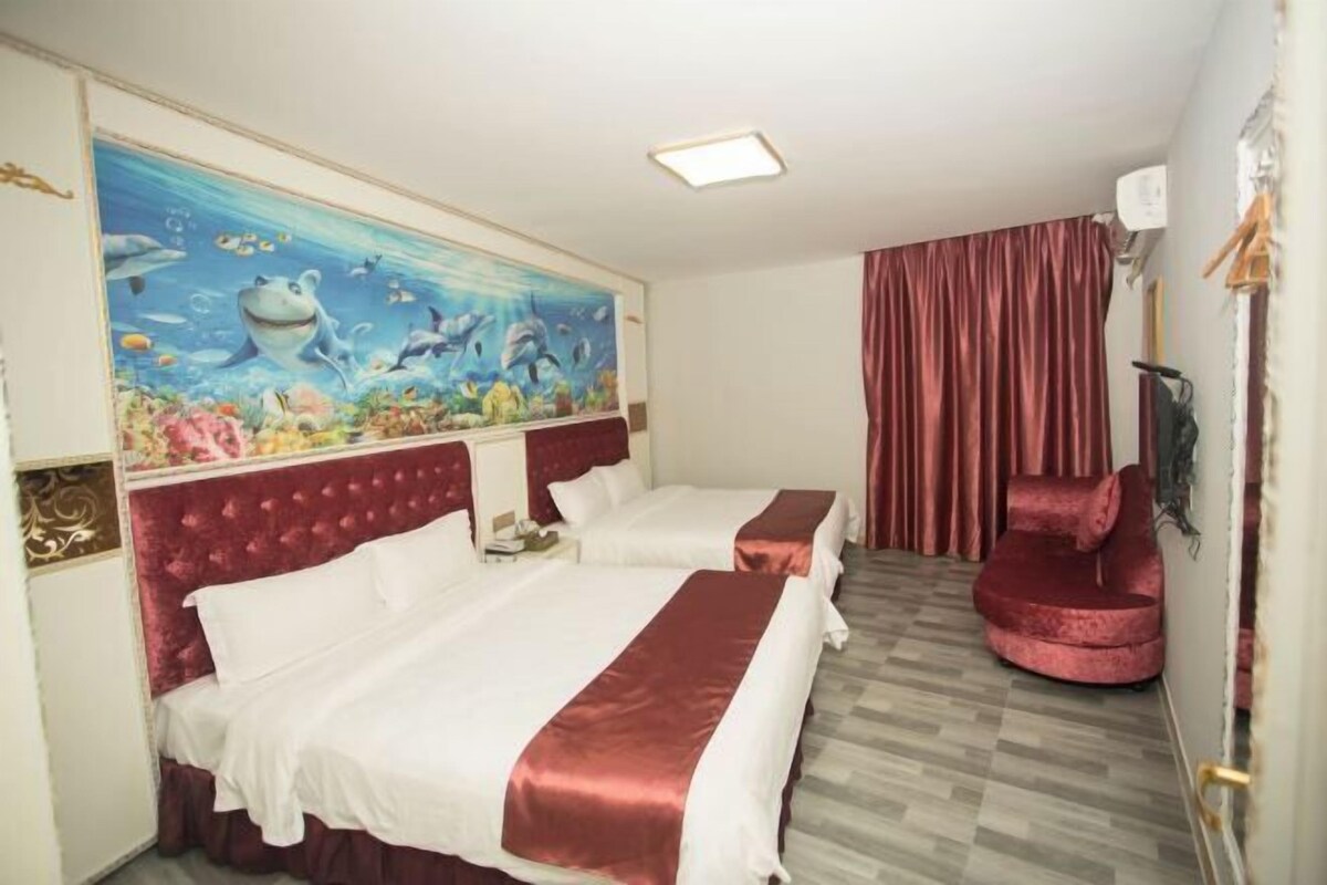 Hotellihuone, jossa on kaksi sänkyä, punainen tuoli, seinämaalaus, jossa on kuvattuna vedenalainen maisema, ja punainen verho.