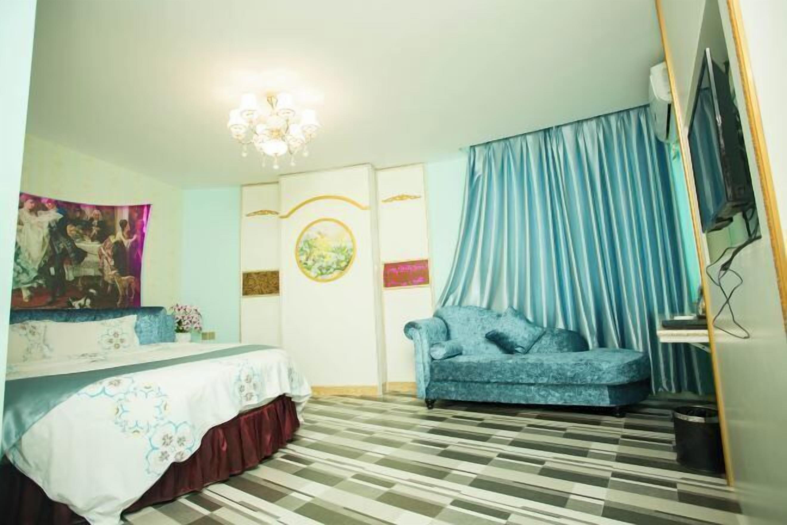 A room with a bed, a sofa, a chandelier, and a television.