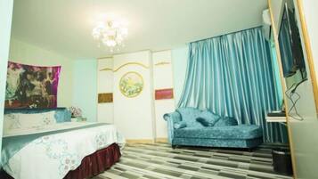 A room with a bed, a sofa, a chandelier, and a television.