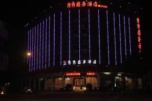 Un hotel con luces de neón verticales y un letrero con caracteres chinos.