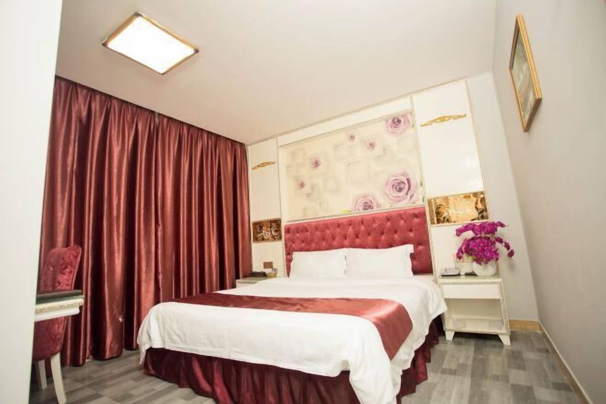 Quarto com cama grande, mesa de cabeceira, cadeira e janela com cortinas.