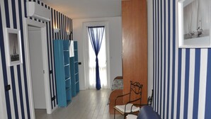 A room with striped walls, a blue sofa, a wooden cabinet, and a bed with a blue curtain. - Poolside Stay in Lazise (Lazise)