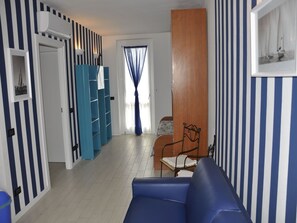 Ein Zimmer mit Streifenmuster an den Wänden, einem blauen Sofa, einem Holzkabinett und einem Bett mit blauer Vorhang.