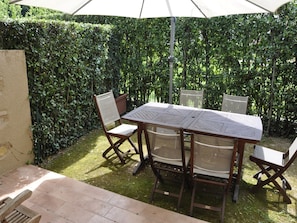 A patio with a table and chairs, surrounded by a hedge.