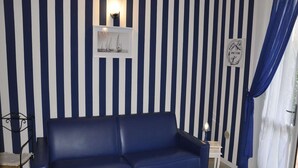 A room with a blue sofa, a small table, a wall-mounted shelf with a picture, and a curtain. - Poolside Stay in Lazise (Lazise)