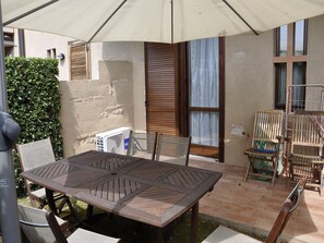 Une terrasse extérieure avec une table et des chaises en bois, un espace abrité et un tuyau d’arrosage.