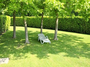 A park with a white bench under trees, surrounded by well-maintained grass and hedges.