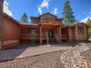 A two-story house with a stone facade, a wooden porch, and a gravel driveway. - Cabin 5 Torreon with Hot Tub (Show Low)