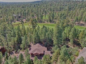 Une maison entourée d’une forêt dense, avec un terrain de golf situé à proximité.