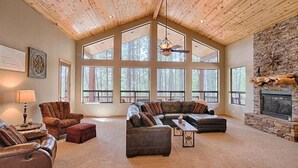 A spacious living room with a high ceiling, large windows, a stone fireplace, and a cozy seating area. - Cabin 5 Torreon with Hot Tub (Show Low)