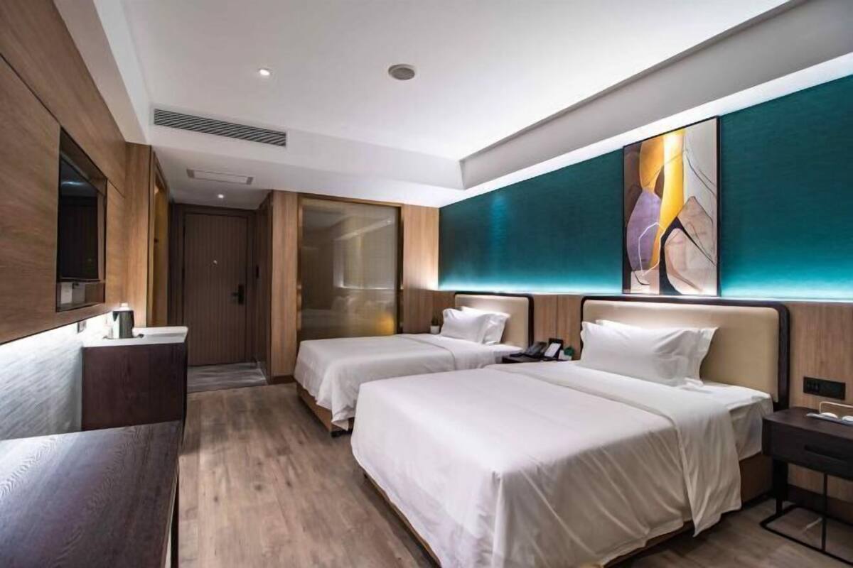 A hotel room with two beds, a desk, a mirror, and a large abstract painting on the wall.