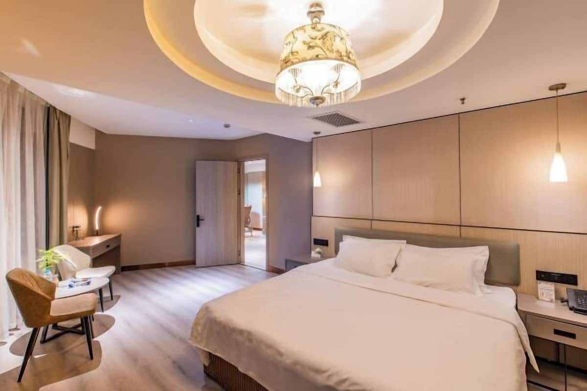 A hotel room with a large bed, a desk, a chair, and a chandelier.
