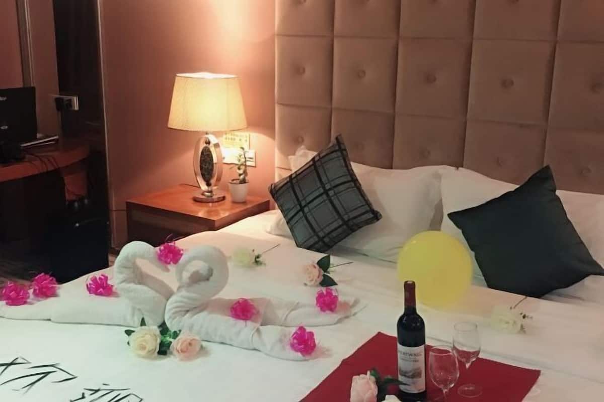 A hotel room with a bed, a nightstand with a lamp, a bottle of wine, and glasses.