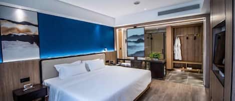 A modern hotel room with a large bed, a nightstand, a desk, a mirror, and a view of the sea.