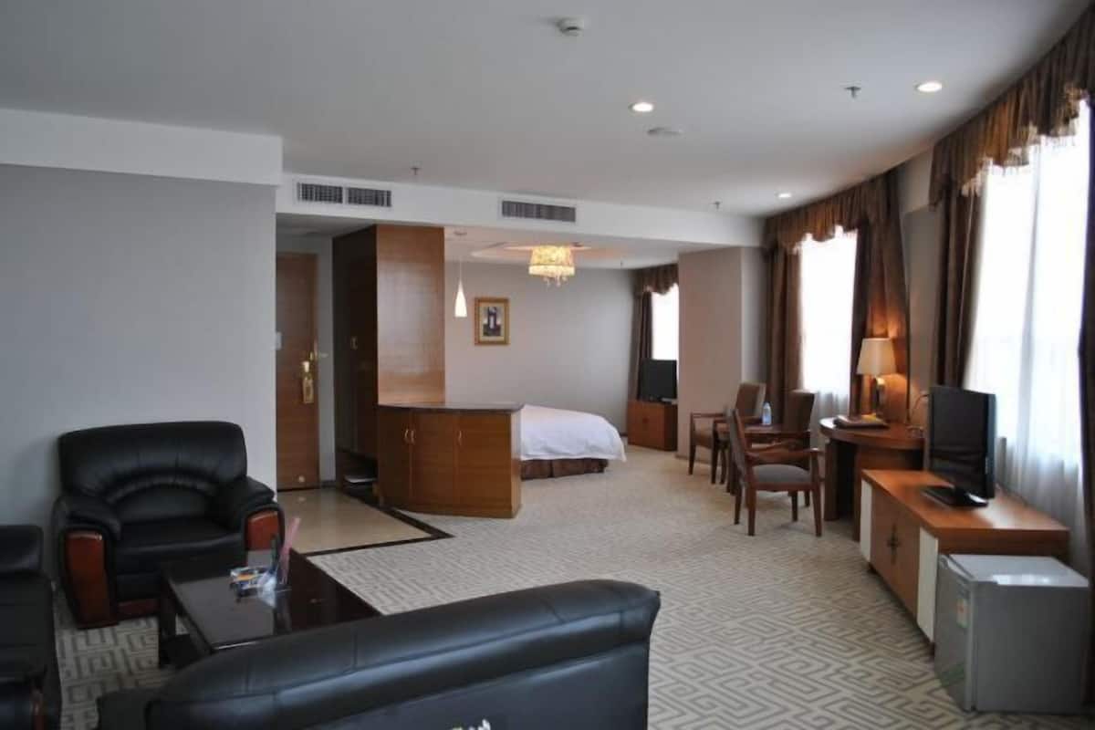 A hotel room with a bed, desk, chair, television, and a small refrigerator.