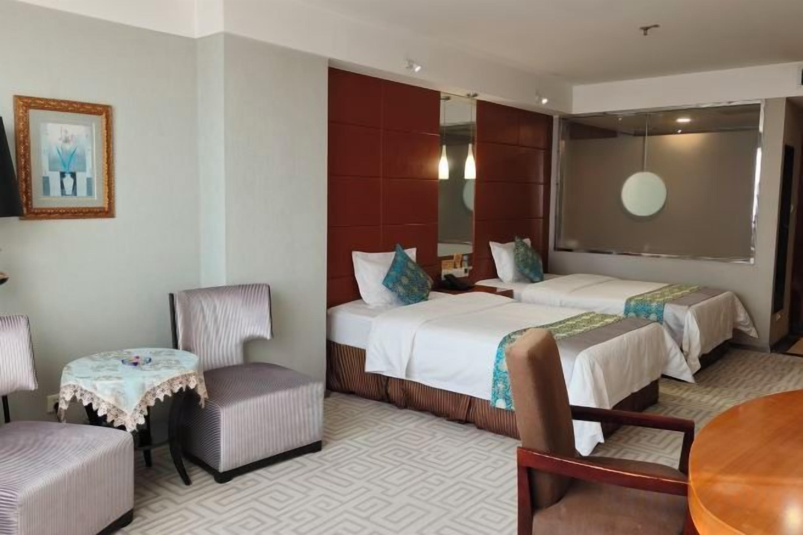 Une chambre d’hôtel avec deux lits, une petite table, une chaise et une grande fenêtre.