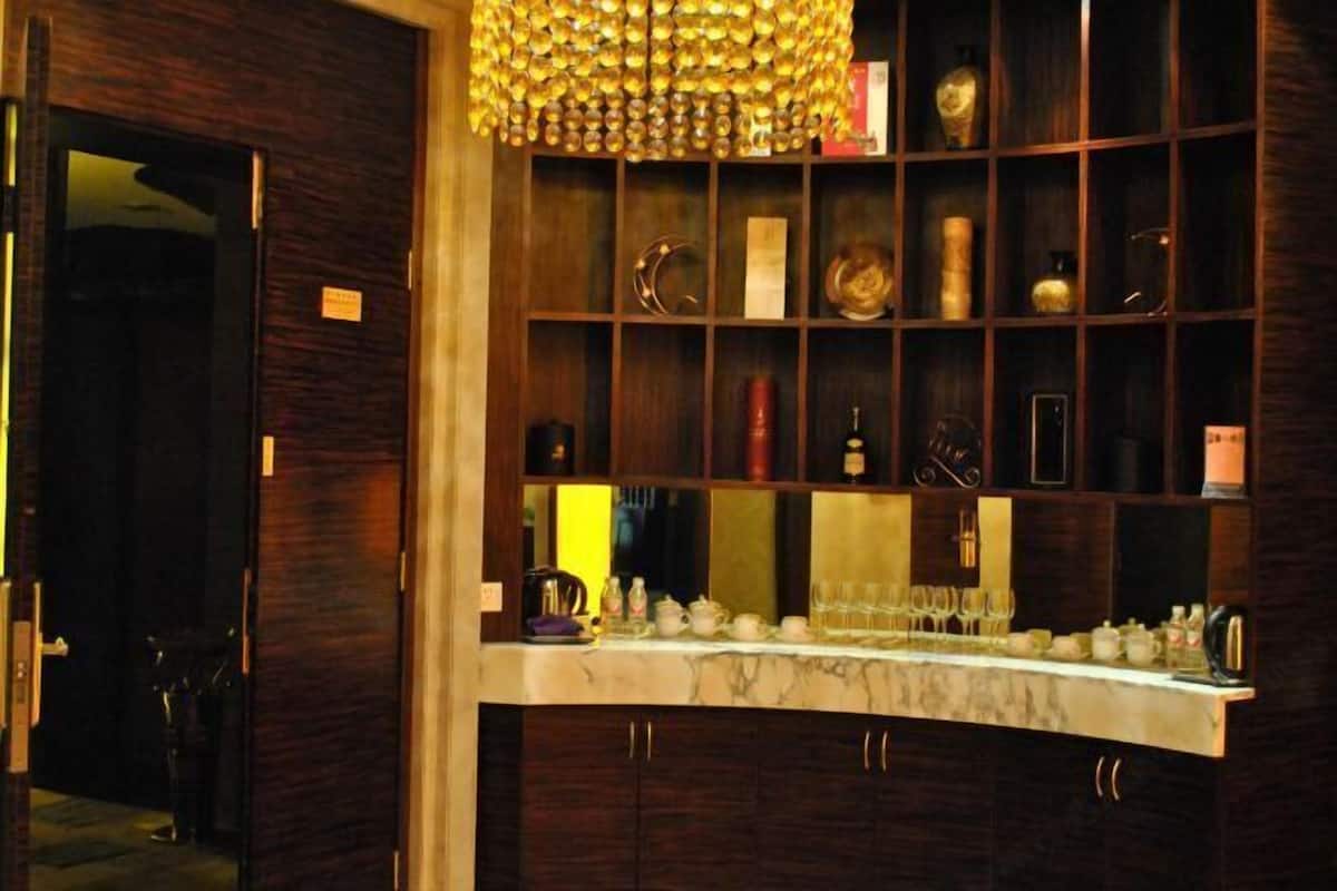 A bar area with a marble countertop, shelves with various bottles and glasses, and a decorative chandelier.