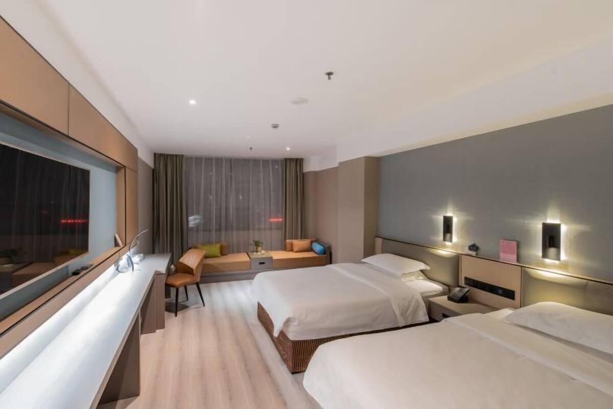 Ein modernes Hotelzimmer mit zwei Betten, einer Sitzecke und einem großen Fenster.