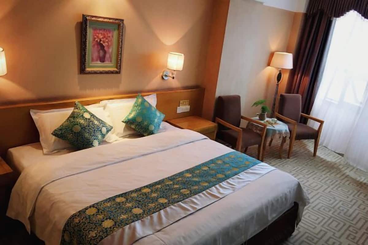 A hotel room with a bed, two nightstands, a desk with a chair, a lamp, and a window with curtains.