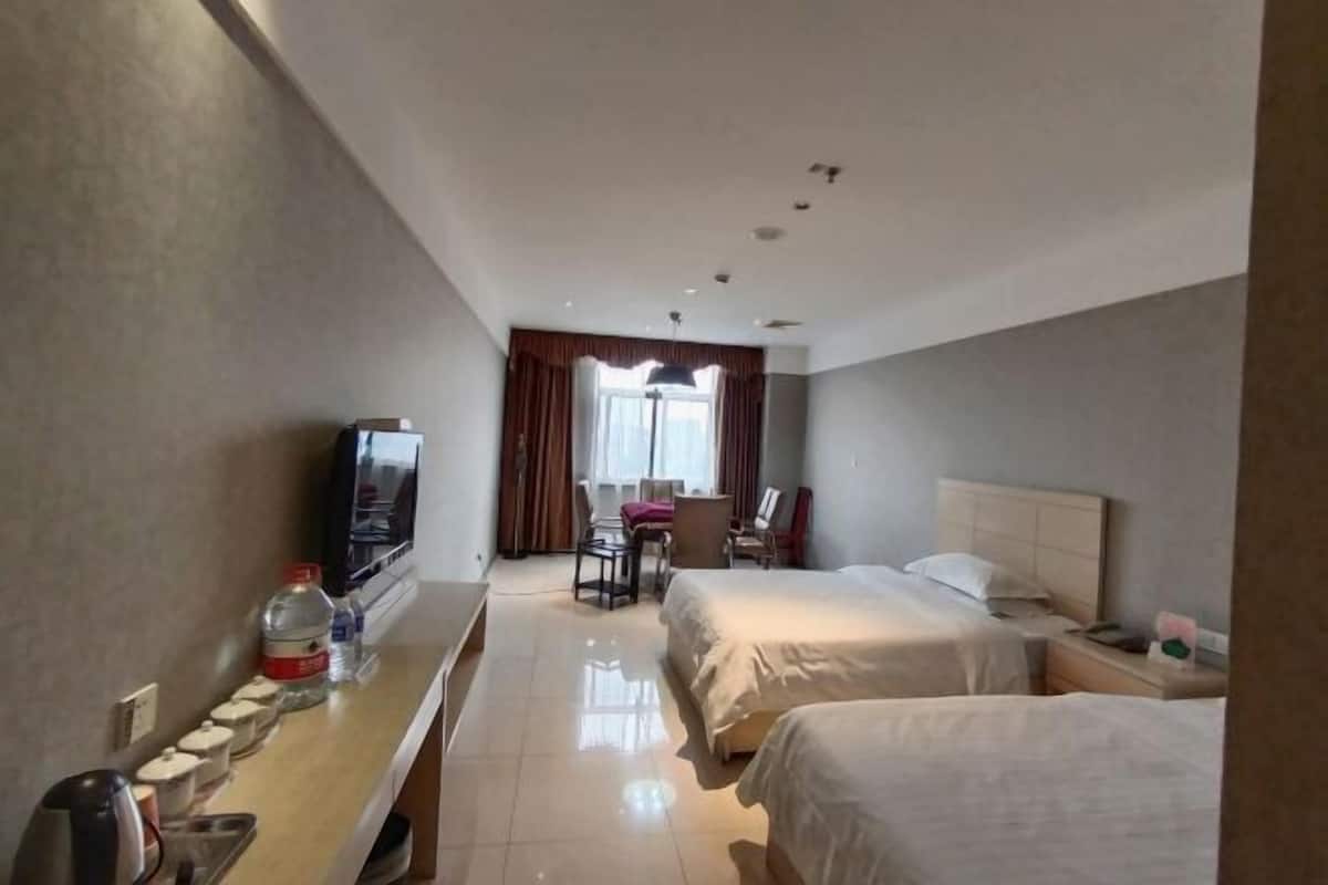 A hotel room with two beds, a desk with a television, a chair, and a window with curtains.