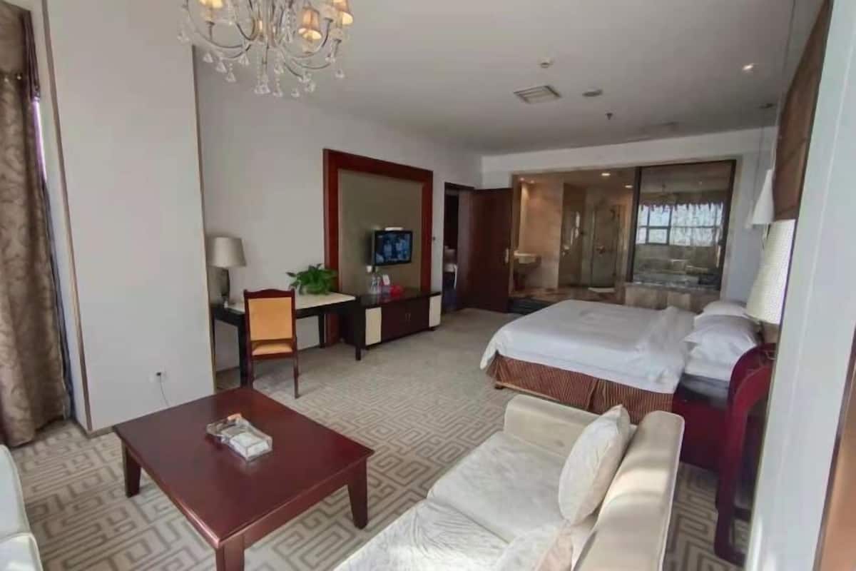 A hotel room with a bed, a sofa, a desk with a chair, a television, and a chandelier.