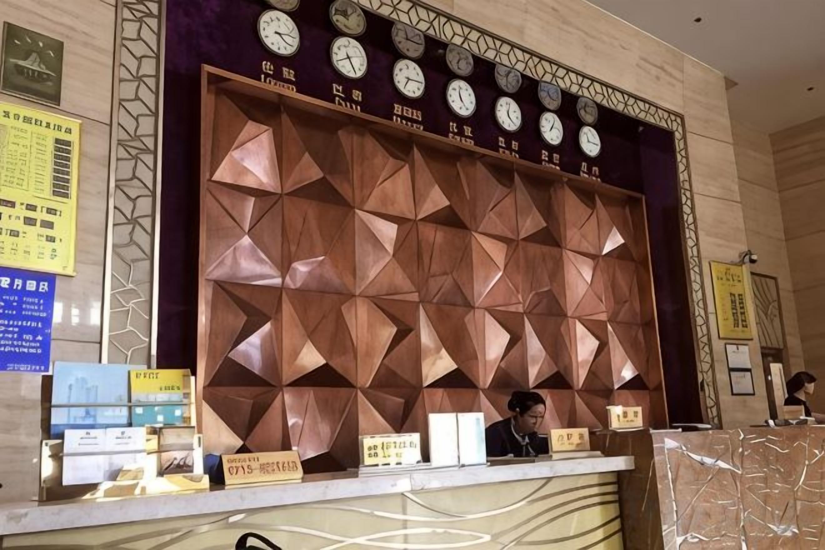 A reception desk with a geometric patterned wall behind it, clocks, and some informational signs.