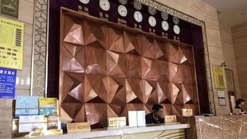 A reception desk with a geometric patterned wall behind it, clocks, and some informational signs.
